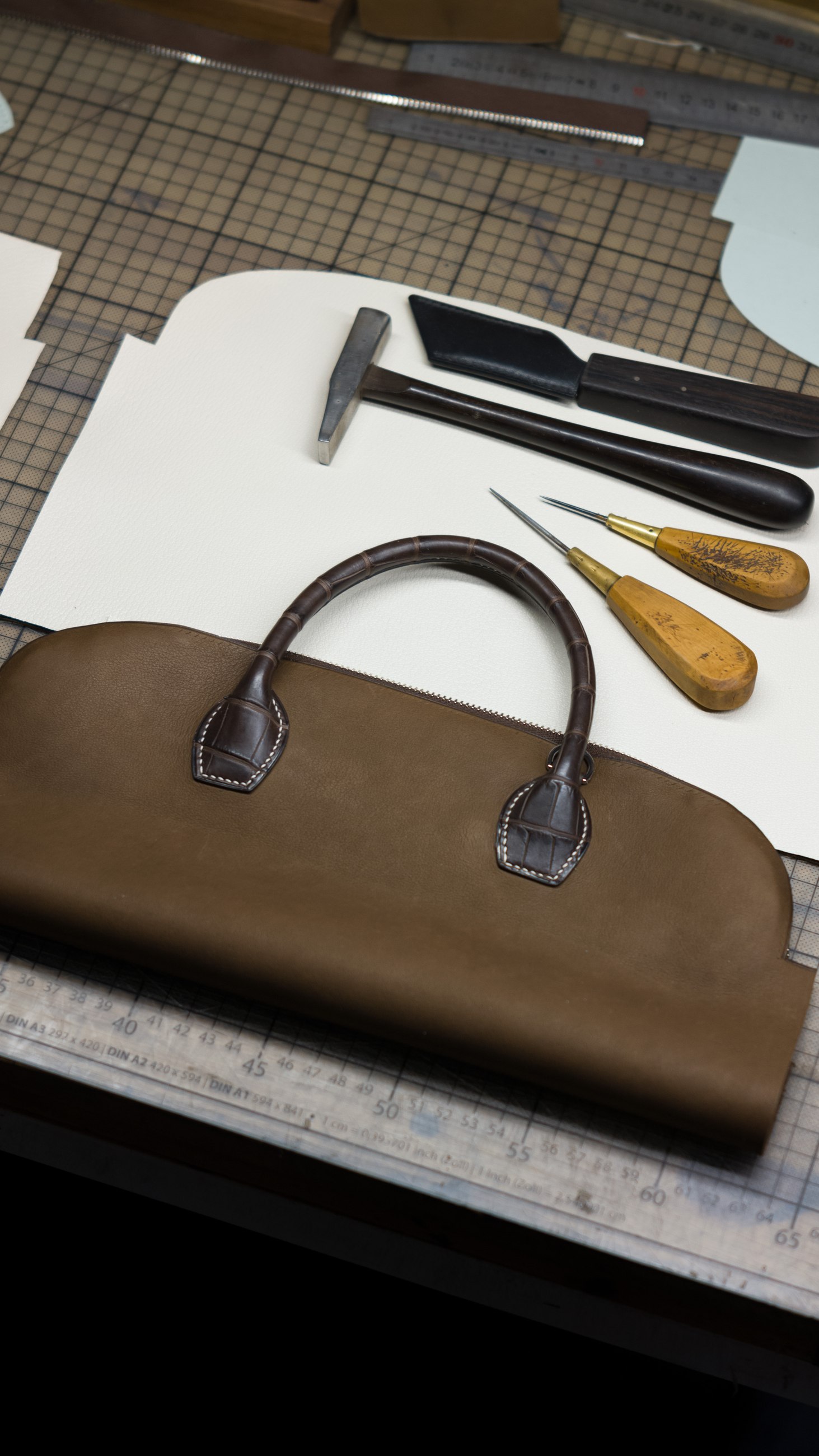 Sac en cuir en cours de fabrication sur l’établi, avec son patron et les outils
